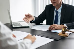 A man and a woman are sitting at a table with papers and a laptop. The man is wearing a suit and tie